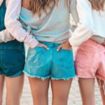 Back view of three young female hipster friends.Girls dressed in summer casual clothes.Women standing outdoors.They put their hands in shorts in back pockets.Posing at sunset